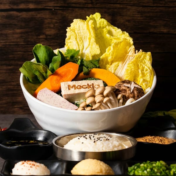 Hot pot ingredients including napa cabbage, vegetables, mushrooms, tofu, dipping sauces, rice, and Mocki-branded tofu arranged on a wooden table.
