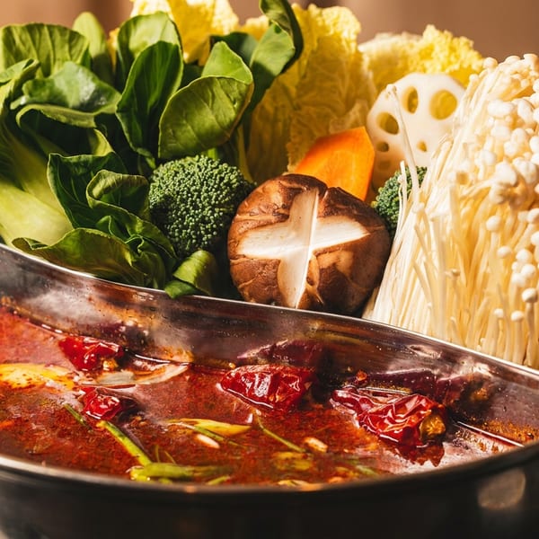 Split hot pot with spicy red broth, leafy greens, broccoli, mushrooms, lotus root, carrots, and napa cabbage.